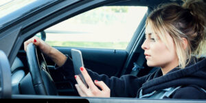 Woman driving black car while texting and not looking at road