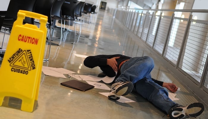 Man laying on floor next to a caution wet sign after a Rhode Island slip and fall injury