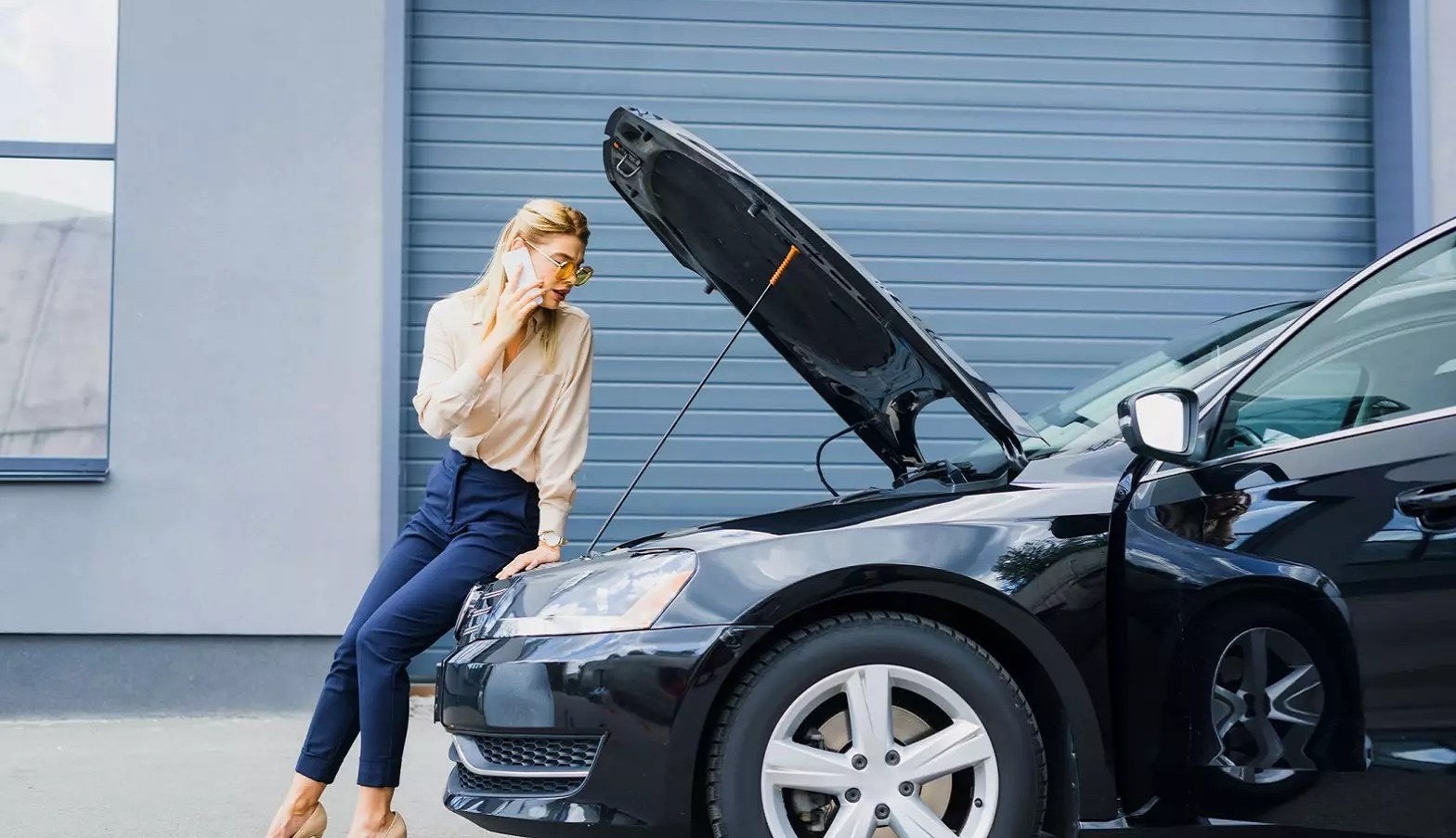 woman standing over open hood of broke down car